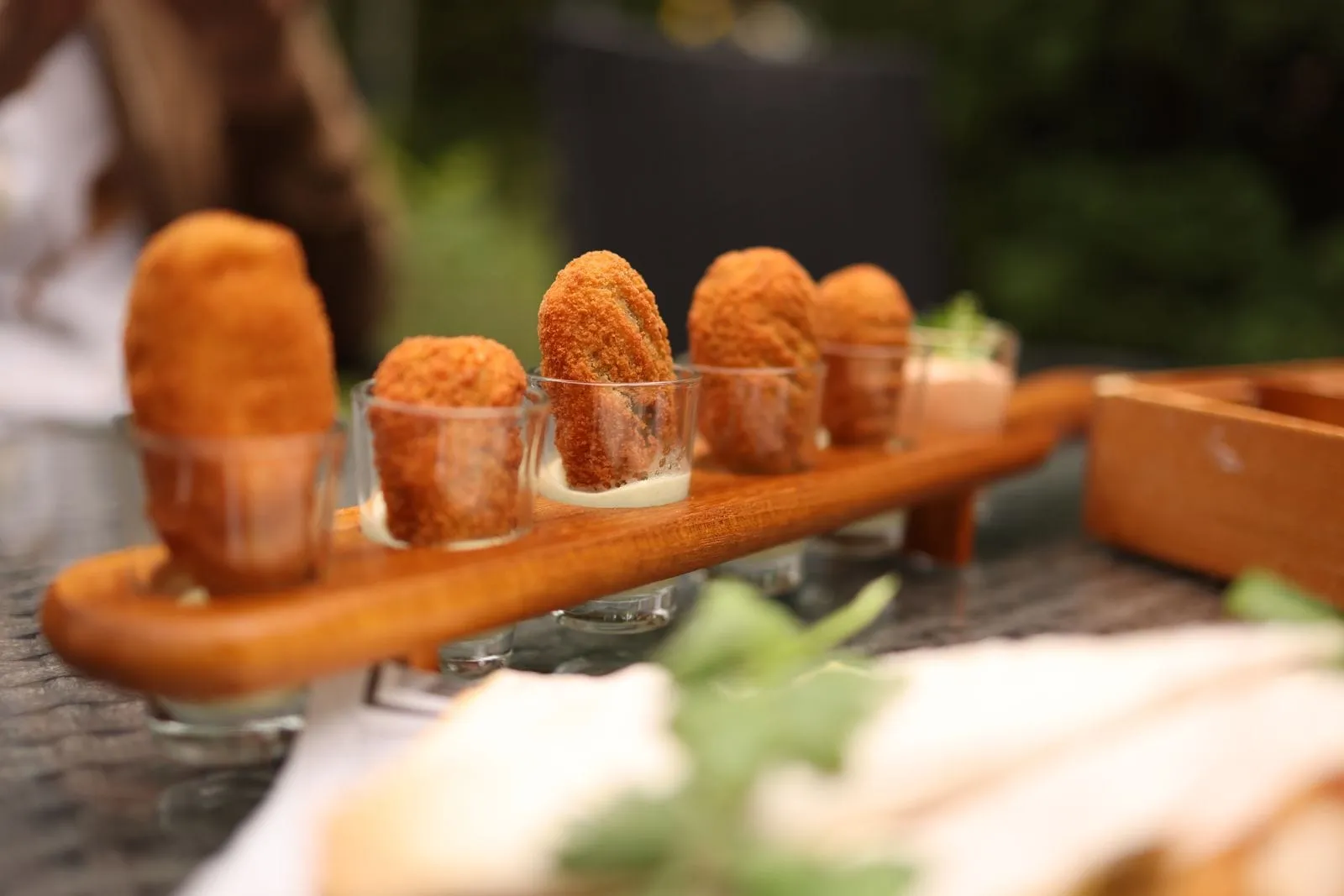 Bouchées panées dorées servies debout dans de petits verres, sur une planche en bois