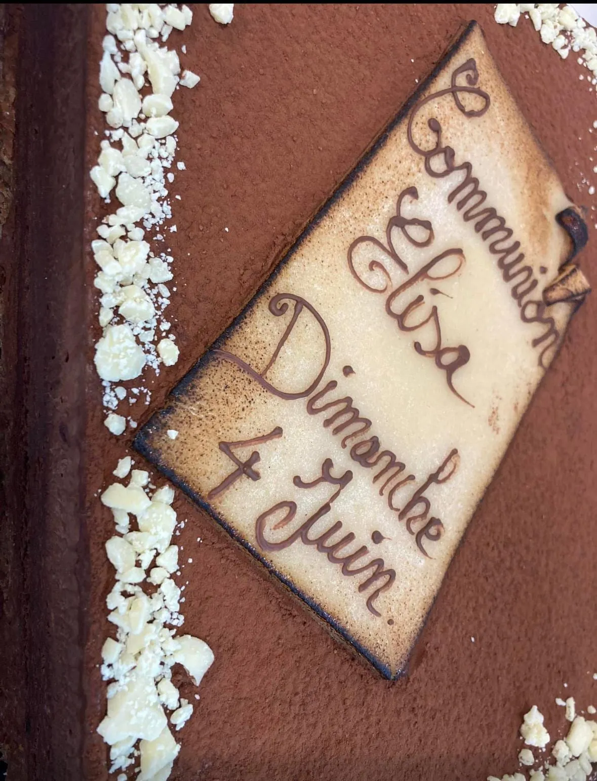 Entremets au chocolat saupoudré de cacao, copeaux de chocolat blanc et plaque décorative écrite au chocolat