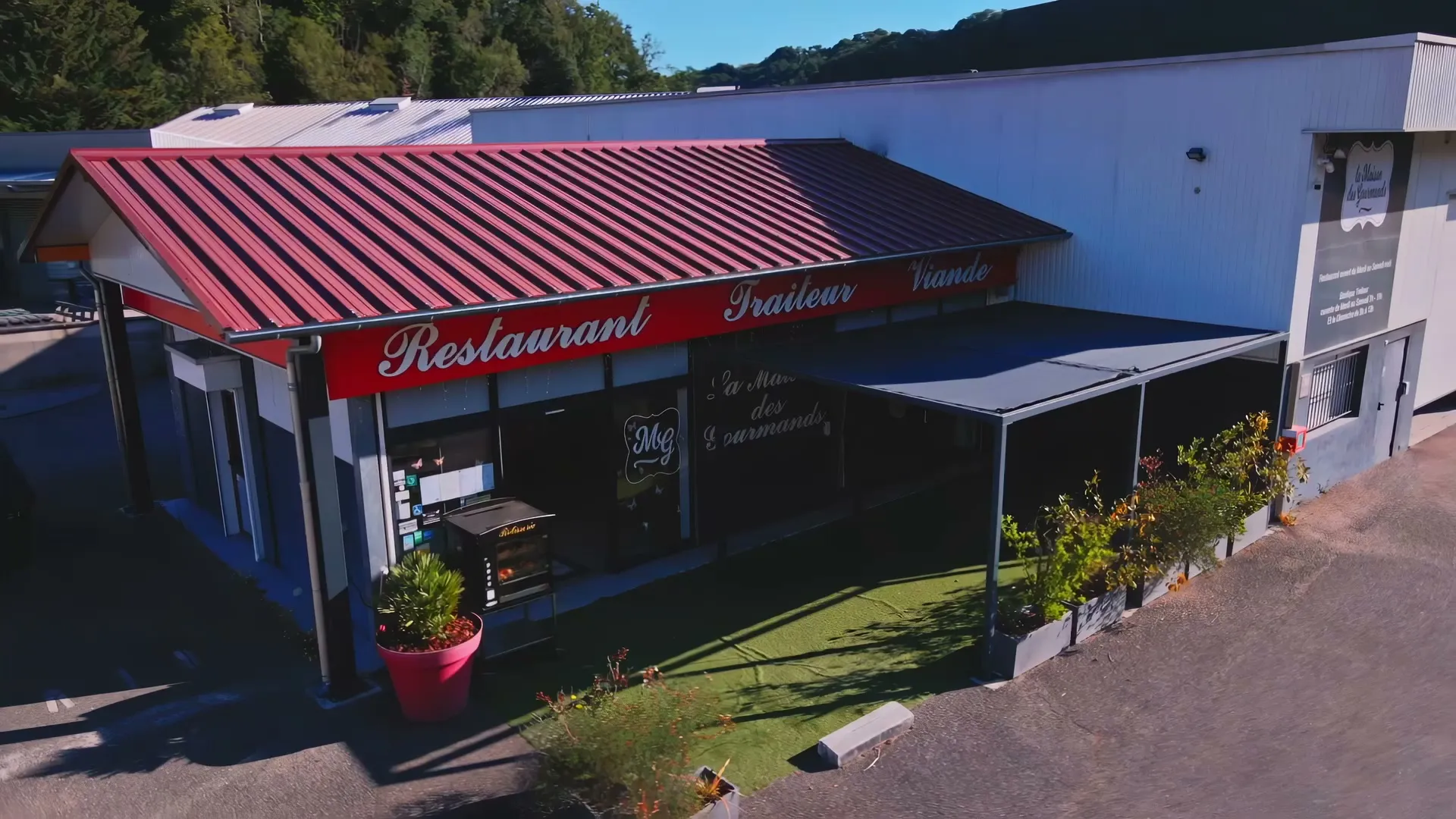 La Maison des Gourmands vue du ciel : le toit rouge, l'enseigne Restaurant Traiteur et la terrasse couverte, au soleil