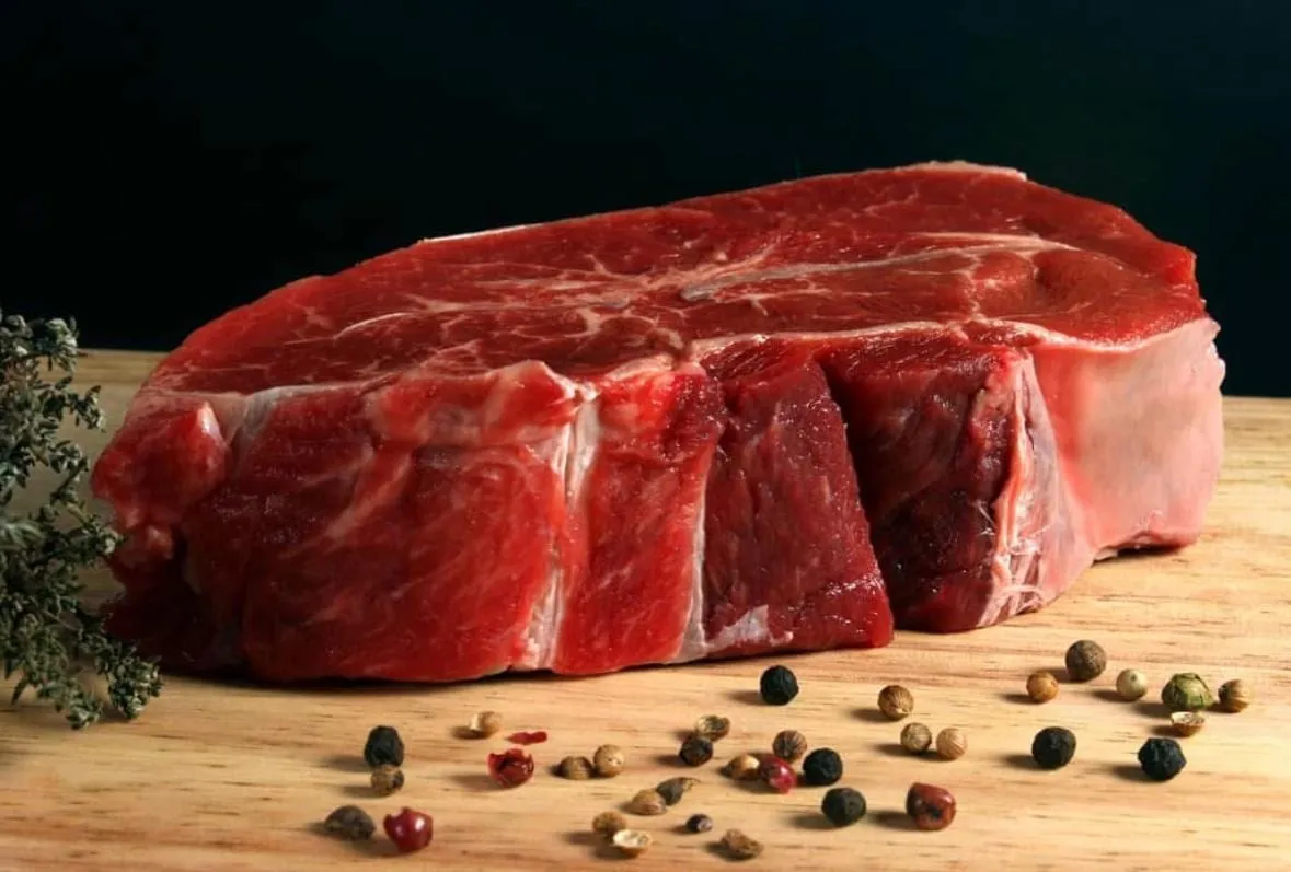 Belle pièce de bœuf sur une planche en bois, poivres en grains et brin de thym