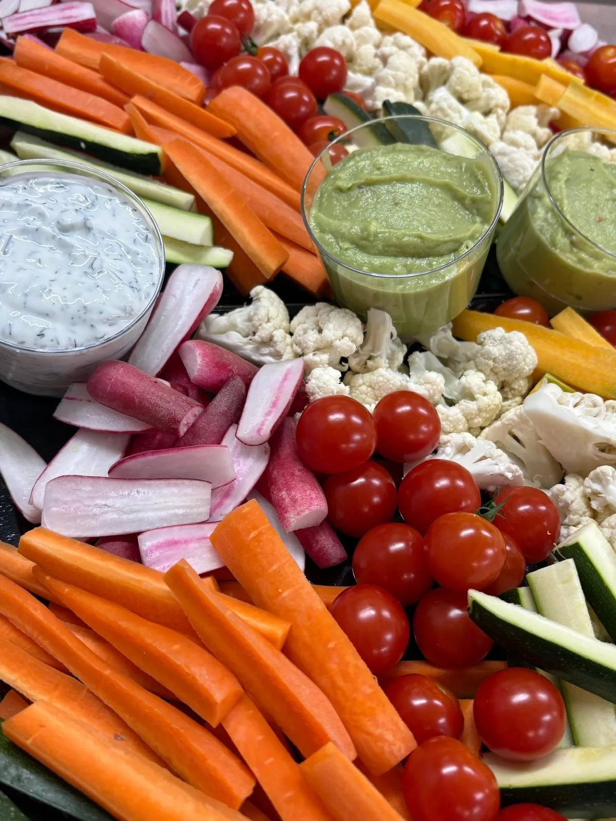 Bâtonnets de carottes, radis, chou-fleur, courgettes et tomates cerises autour d'une crème aux herbes et d'un guacamole