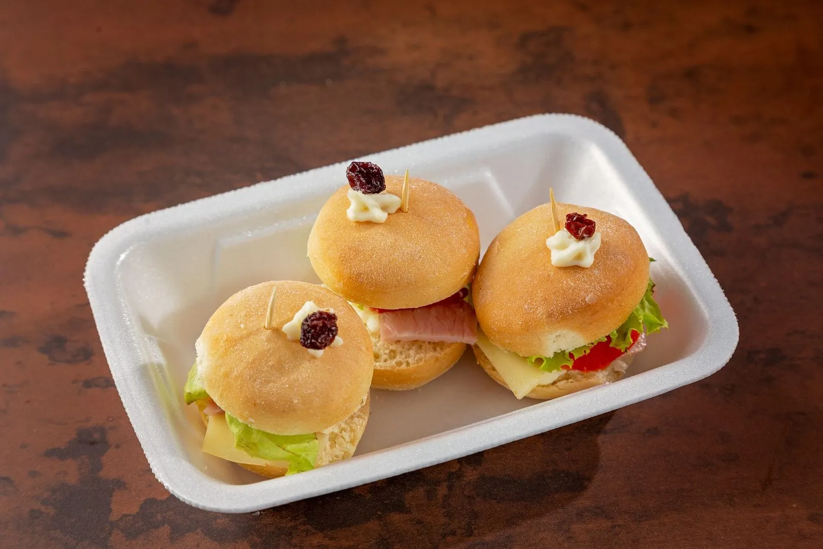 Trois petits pains garnis de jambon et de fromage, sur une barquette