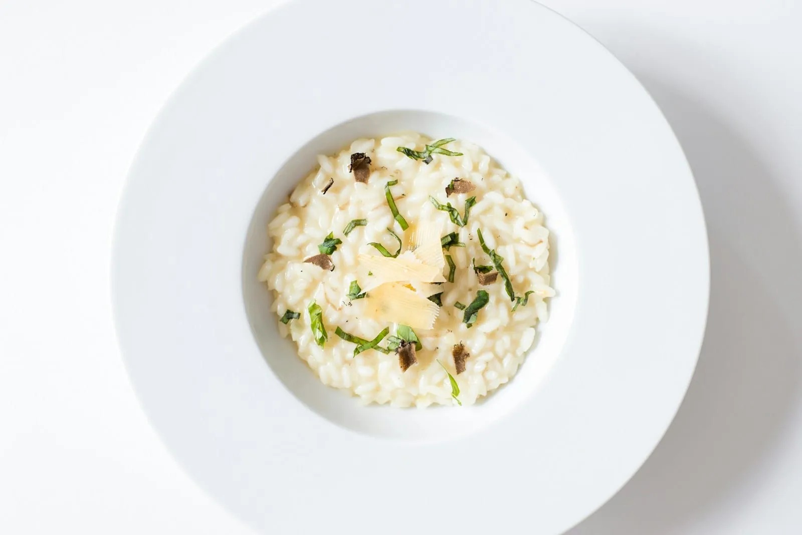 Risotto crémeux et copeaux de parmesan, servi dans une assiette creuse blanche