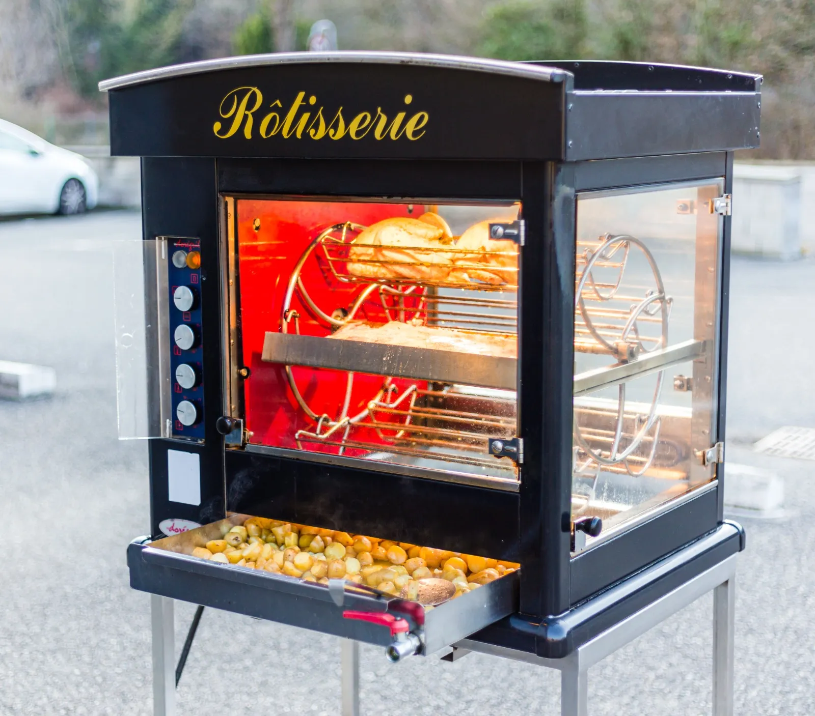 La rôtissoire de la maison en plein air : volailles à la broche et bac de pommes de terre qui dorent dans le jus