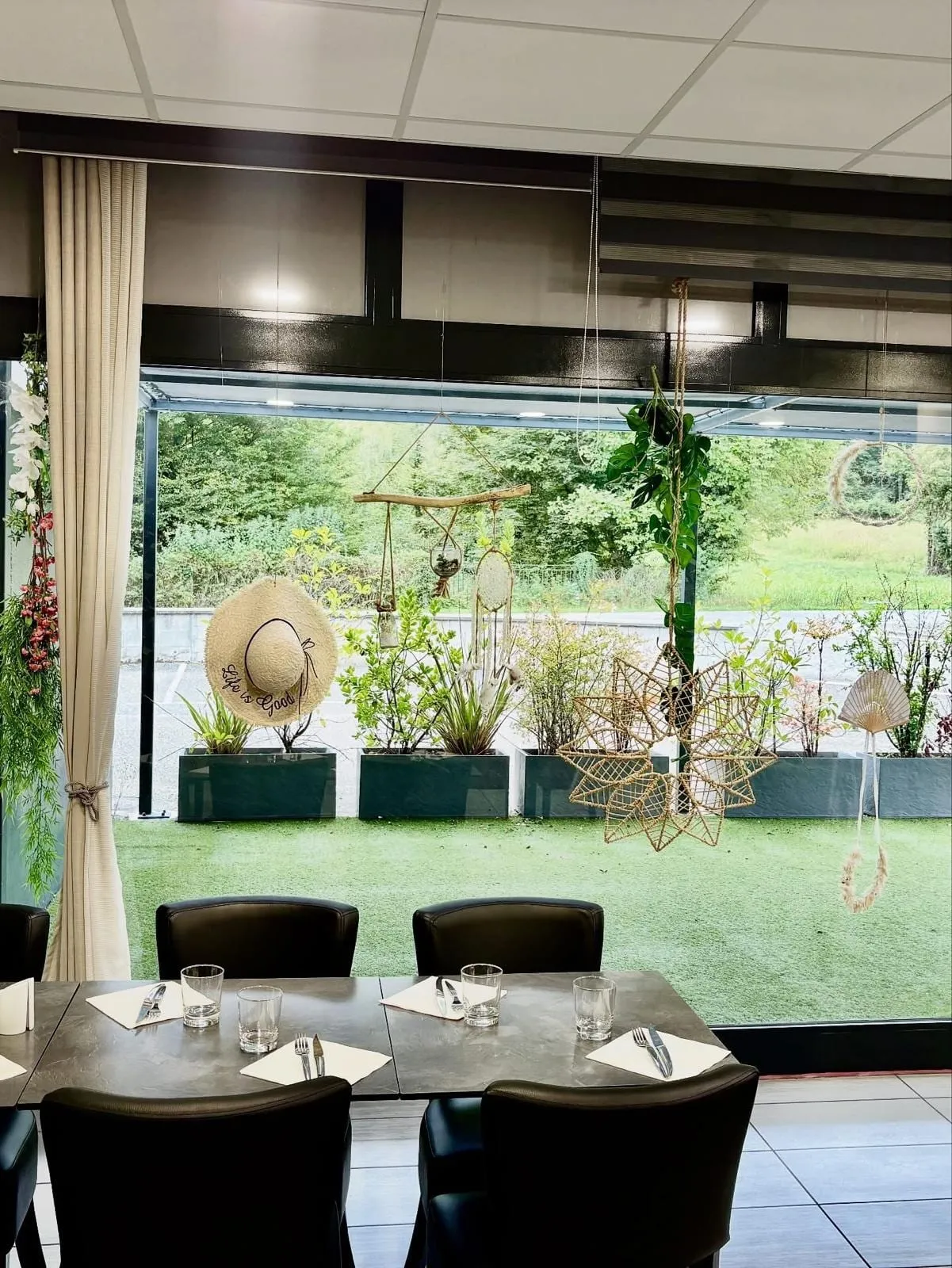 La salle du restaurant ouverte sur la terrasse par la baie vitrée, plantes et décorations suspendues
