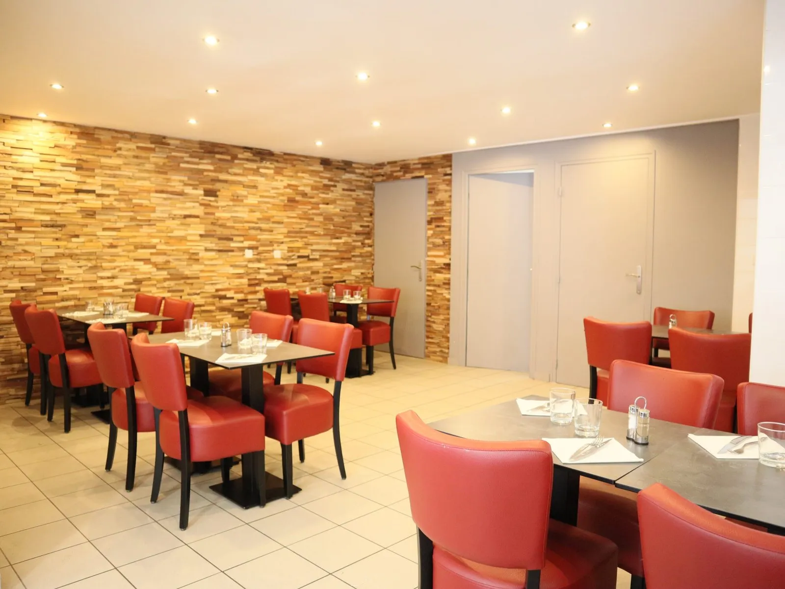 La salle du restaurant : grand mur de bois, fauteuils de cuir rouge et tables noires