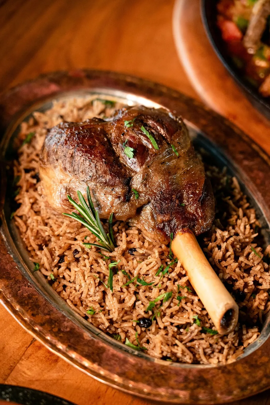 Souris d'agneau rôtie, os apparent et brin de romarin, servie sur un lit de riz épicé