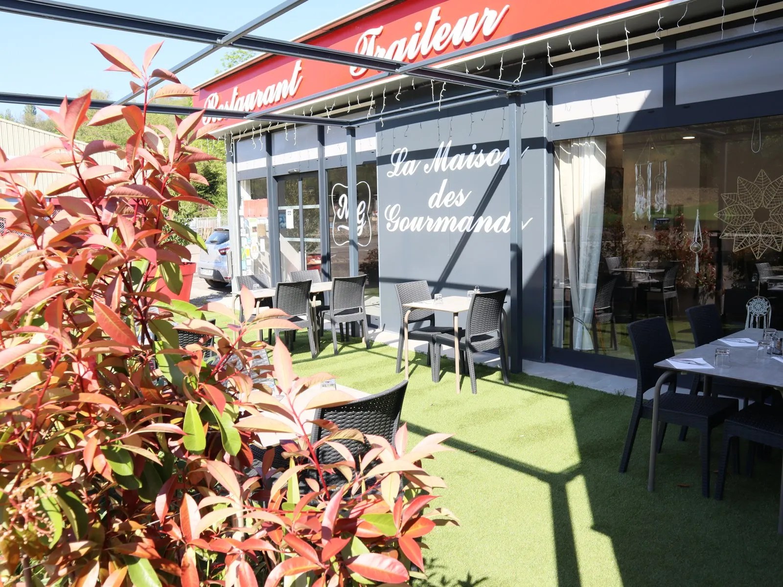 La terrasse vue à travers les feuilles rouges du photinia, tables et chaises tressées