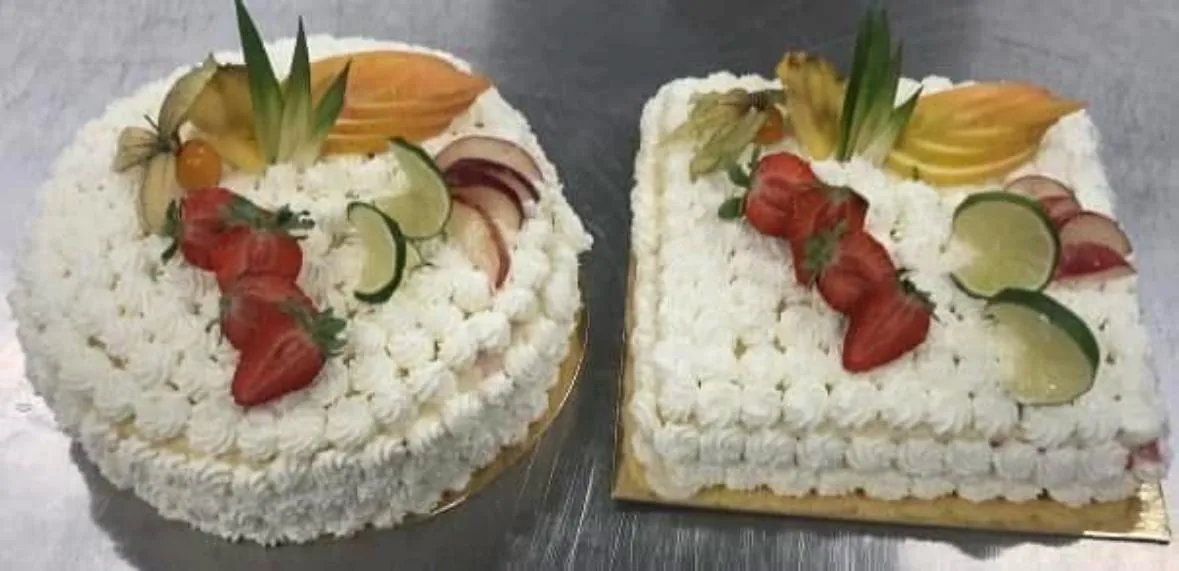 Deux gâteaux crémés, rond et carré, décorés de fraises, de citron vert et de fruits